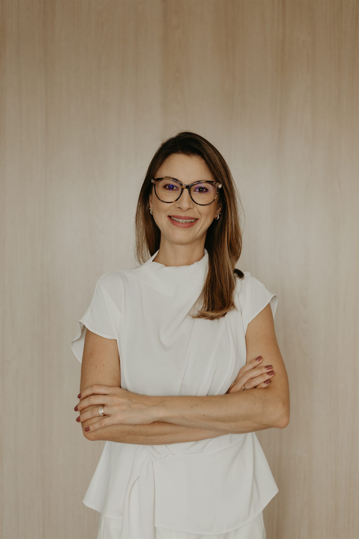 Rafaela Gualdi, psicóloga clínica, sorrindo com os braços cruzados no consultório.